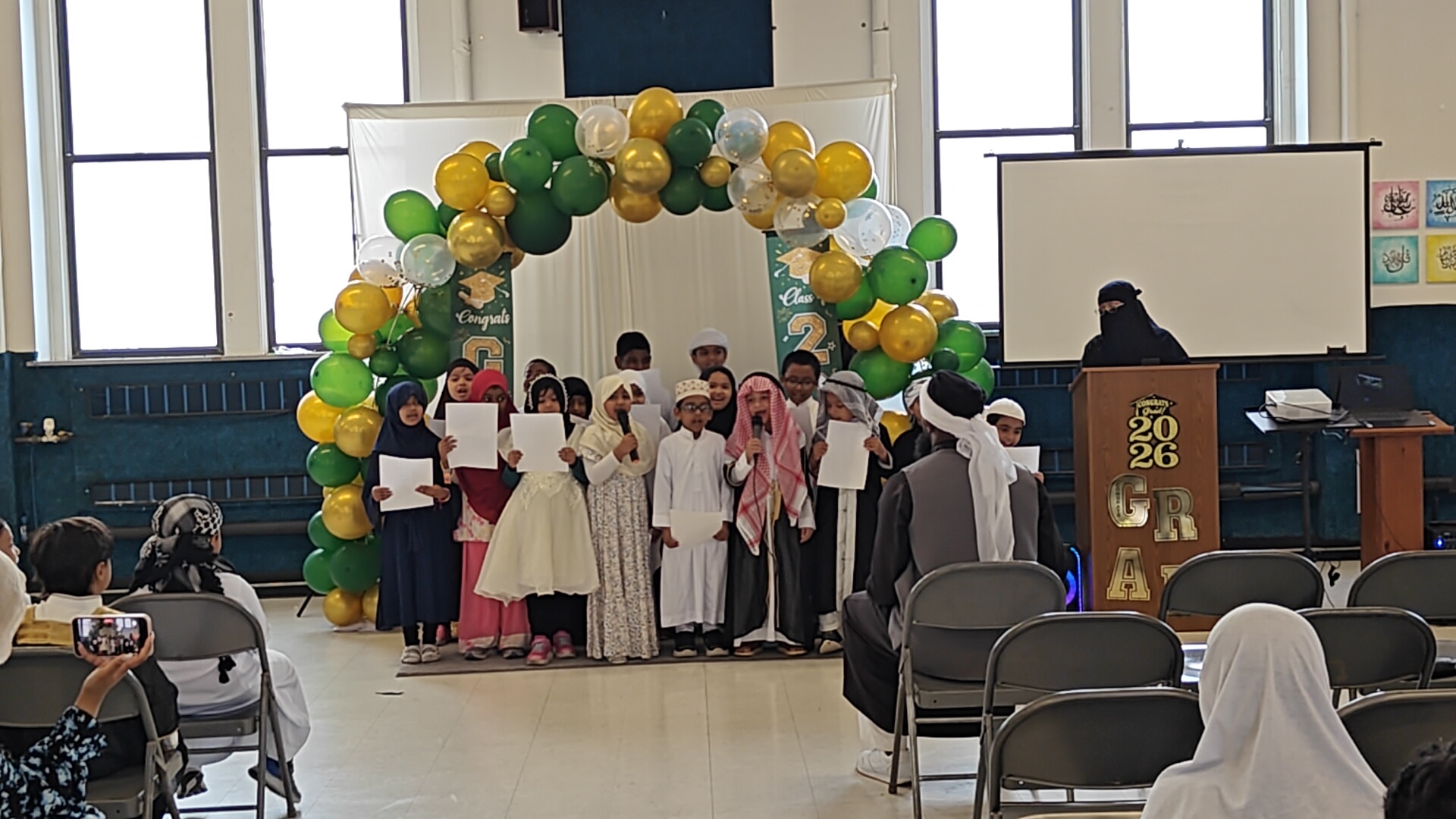 Students at graduation beneath a green and gold balloon arch