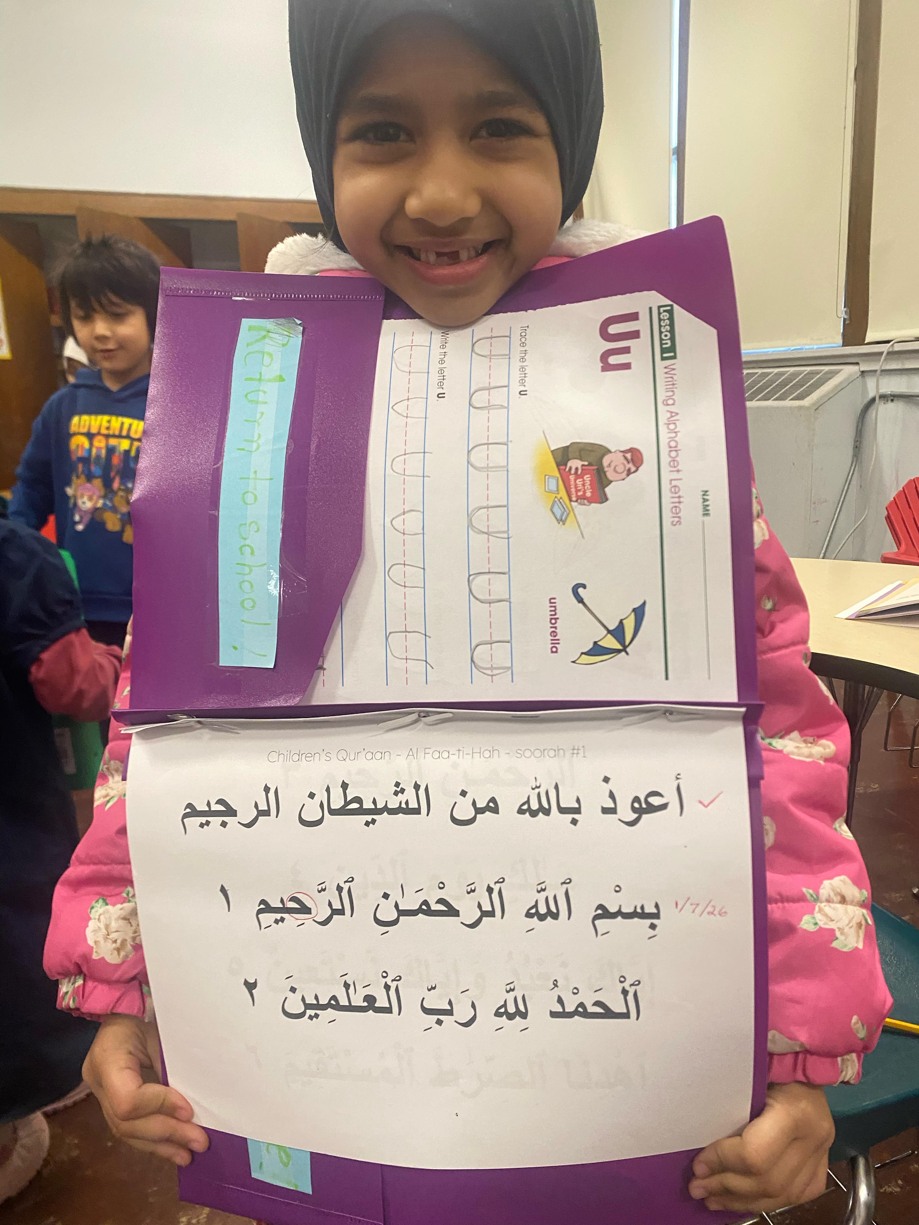 Student showing Quran and alphabet work